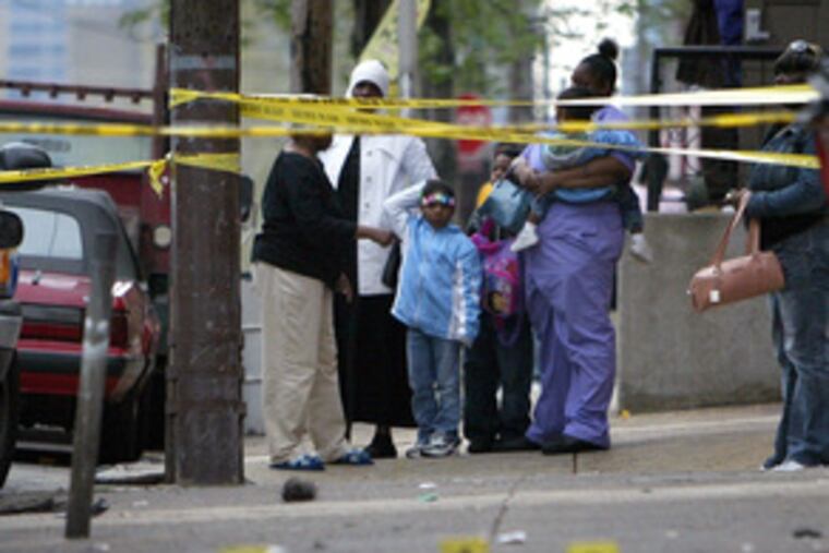Neighbors look down a sidewalk covered with evidence markers Saturday as police investigate a homicide at 19th Street and Girard Avenue.