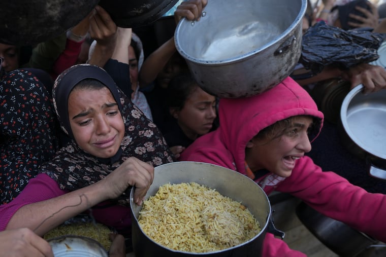 Palestinian girls struggle to reach for food at a distribution center in Khan Younis, Gaza Strip, on Dec. 6. As of now, there is no visible Israeli effort to improve the humanitarian disaster in Gaza and surge aid in, writes Trudy Rubin.