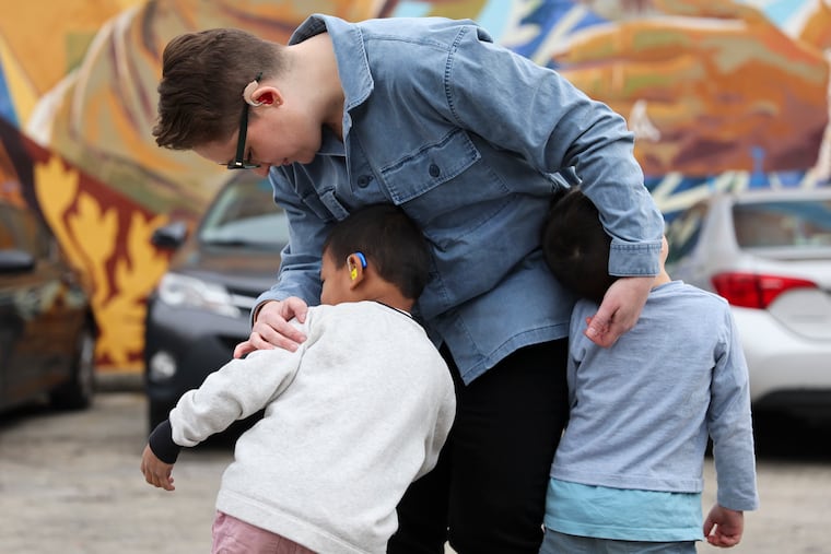 Sara Nović poses for a portrait with her two sons, ages 5 and 4, near a mural on Germantown Avenue in Philadelphia on Monday, Feb. 12, 2024. Nović, who is deaf, has concerns about the recent CHOP gene therapy trial that cured a boy of hearing loss.