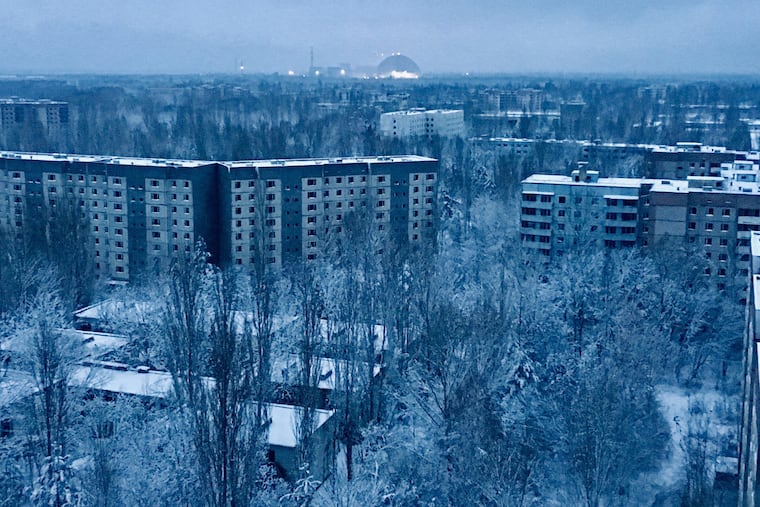 On the roof of a 16-story apartment building in Pripyat at sunset, a visitor can see what remains of the abandoned town. The only light comes from the Chernobyl nuclear station and the giant containment shield covering the remains of the exploded reactor.