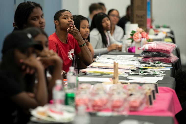 Shahad Lockhart, in red, watches as people speak about their products and businesses during a pitch competition at a youth entrepreneurship expo at the Philadelphia School District headquarters in Philadelphia, PA on Friday, Aug. 02, 2019. The students of Rebel Ventures, the youth business that's sold more than 1 million of breakfast snack cakes, hosted the expo.