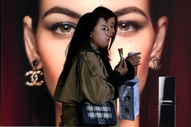 Women eating snacks walk by a Chanel cosmetic shop at a shopping mall in Beijing.