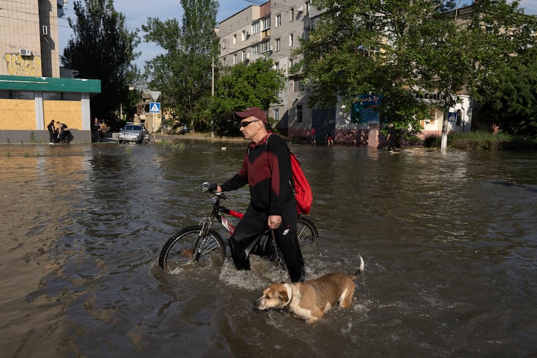 A local resident with a bike and a dog walks along the street past buildings in Kherson, Ukraine, on Tuesday, which were flooded after the Kakhovka dam was destroyed overnight.