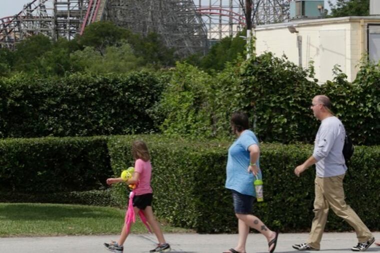 The Texas Giant roller coaster ride sits idle as people walk nearby looking from outside the Six Flags Over Texas park Saturday, July 20, 2013, in Arlington, Texas. Investigators will try to determine if a woman who died while riding the roller coaster at the amusement park Friday night fell from the ride after some witnesses said she wasn't properly secured.(AP Photo/LM Otero )
