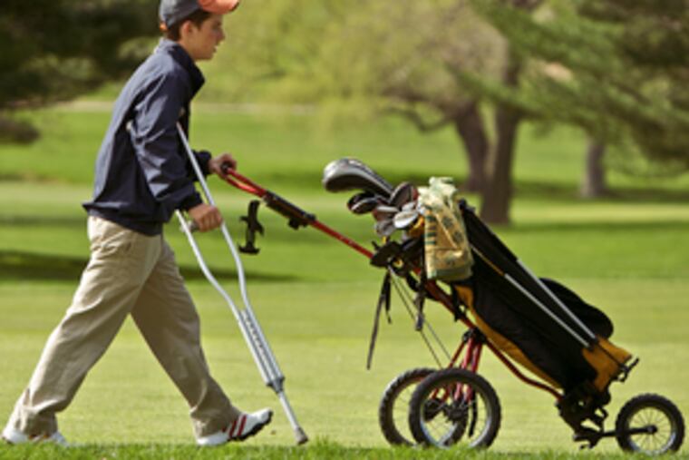 Episcopal Academy's Hunter Hanson pushes his cart with one hand and holds his crutch with the other on the golf course.