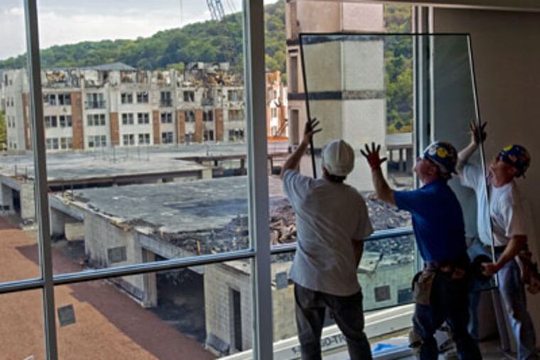 Glaziers (from left) Michael Falasca, Matt Baxter and Tom Nailly, install a replacement window in Millennium Three, the office building next to the partially-built Riverwalk apartment complex that went up in flames last month in Conshohocken. Millennium Three needed 107 windows and 8 metal frames replaced due to the extreme heat of the fire next door. Not much has been done to the fire-damaged apartment buildings, which can be seen out the windows. (Clem Murray / Inquirer)
