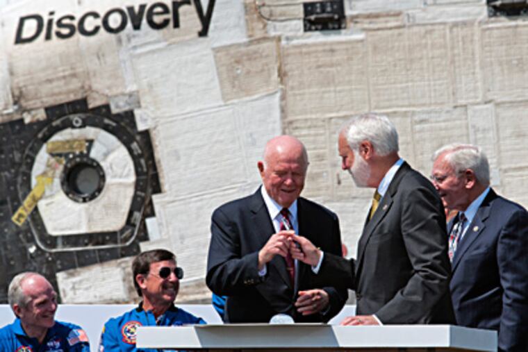 Former astronaut and Sen. John Glenn, center, accepts a pen before signing the handover paperwork as the space shuttle Discovery is officially welcomed to the Udvar-Hazy center in Dulles, Va. Handing him the pen is Smithsonian Secretary Wayne Clough. At far right is Air and Space Museum Director J.R. Dailey. (BILL O'LEARY / The Washington Post)