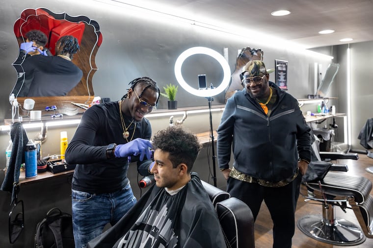 Barber Darnell Washington, 29, (left) and the barber known as Silver Da Barber, 45, (right) consult on this high school student's haircut inside of Philly Fades 2 barbershop located on South Street in Philadelphia. The barbers often cut the hair of many people from different age groups and backgrounds.