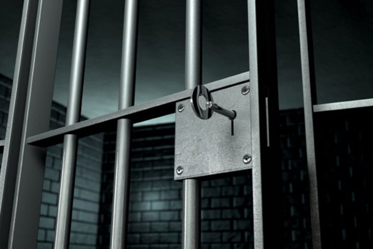 A closeup of the lock of a brick jail cell with iron bars and a key in the locking mechanism with the door open.