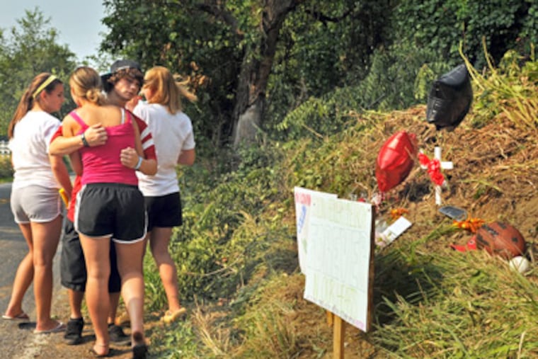 Tyler Wales hugs Brittany Alison (back showing) on Sunday after Alison, Kelsey Brinton (left) and Mandi Geckle (right) brought balloons and signs to a memorial. Four of their classmates died there in a crash overnight. (Tom Gralish / Staff Photographer)