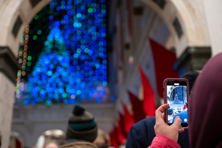 A person records a video of the Wanamaker Light Show on their phone at the Wanamaker Building on Saturday. The light show returns this year after the closing of Macy’s, but it is uncertain if the light show will be able to return next year.