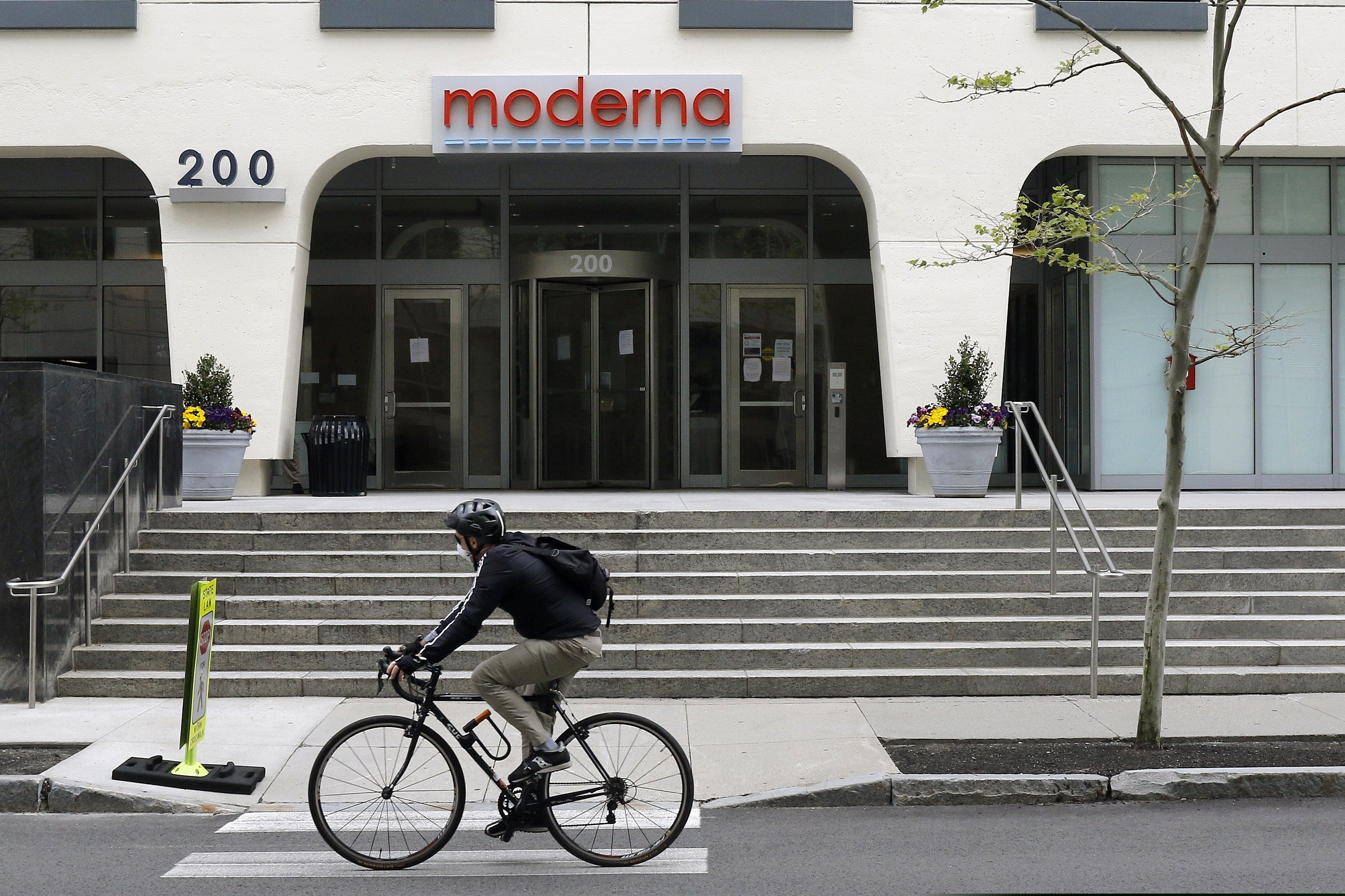 A bicyclists pedals past an entrance to a Moderna, Inc., building, in Cambridge, Mass. Moderna announced Monday that is has begun a pivotal clinical trial of its coronavirus vaccine, the final hurdle before regulatory approval.