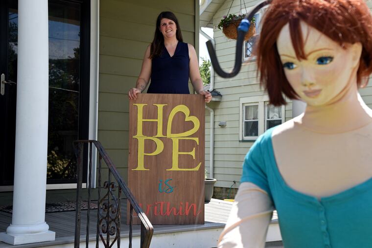 Sara Joy Kuhlen poses on her Audubon, NJ, porch as her creation, a mannequin named 'Hope A. Bounds,' poses in the front yard. A music therapist and mother of two, Kuhlen designed and built Hope and dresses her in a wide range of outfits, drawing smiles from people passing -- and plenty of attention on social media.