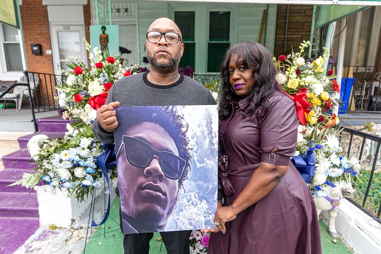 Thomas Blackwell VI and his wife, Sajda, pose for a portrait in front of their West Philadelphia home last month holding a photo of Charles Edward Blackwell II.