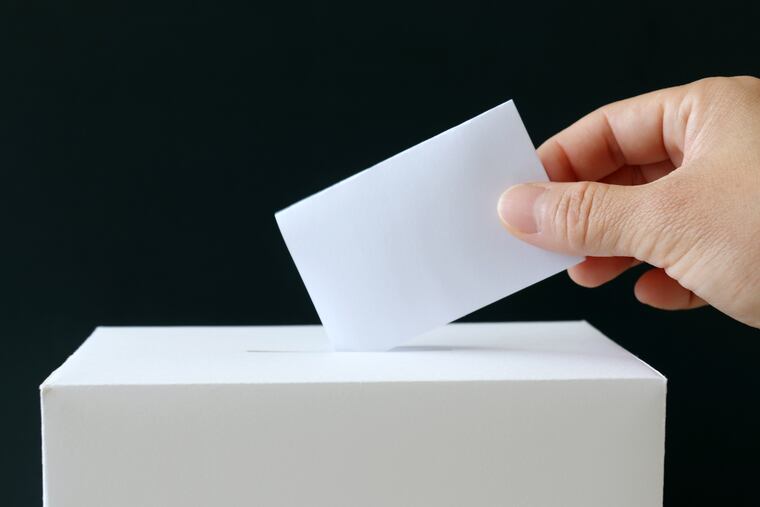 The hand of a woman putting a ballot in the ballot box. Close-up image of ballot and the ballot box.