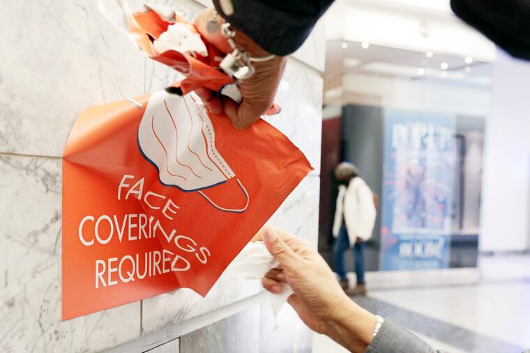 Paula Johnson removes a “Face Coverings Required” sign from Liberty Place in Center City in early March. Johnson works for Arthur Jackson Janitorial Services and — once city officials and her bosses gave the go ahead — she removed a total of nine signs from the Liberty Place property. Philadelphia is no longer requiring masks to be worn indoors.