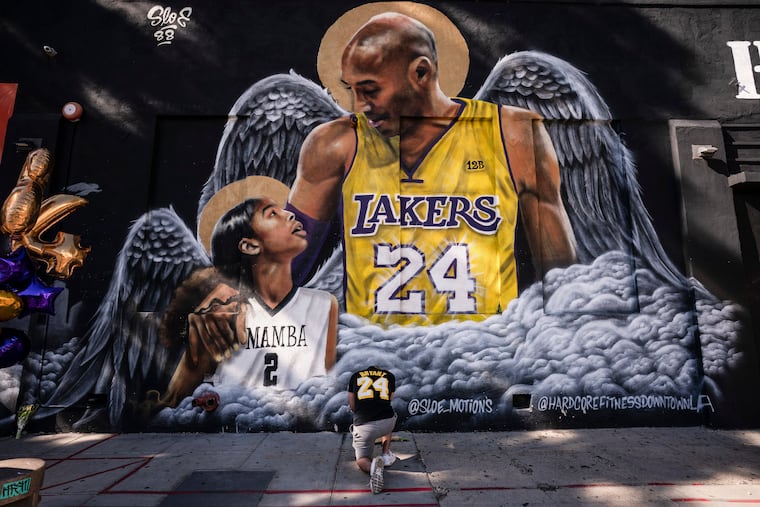 Adam Dergazarian, bottom center, pays his respect for Kobe Bryant and his daughter, Gianna, in front of a mural painted by artist Louie Sloe Palsino, Tuesday, Jan. 26, 2021, in Los Angeles. Bryant, his daughter, and seven other people died in a helicopter crash last year.