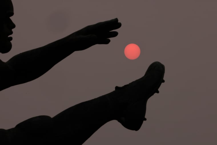 An orange sun goes down behind “The Punter” statue on Wednesday near Citizens Bank Park.