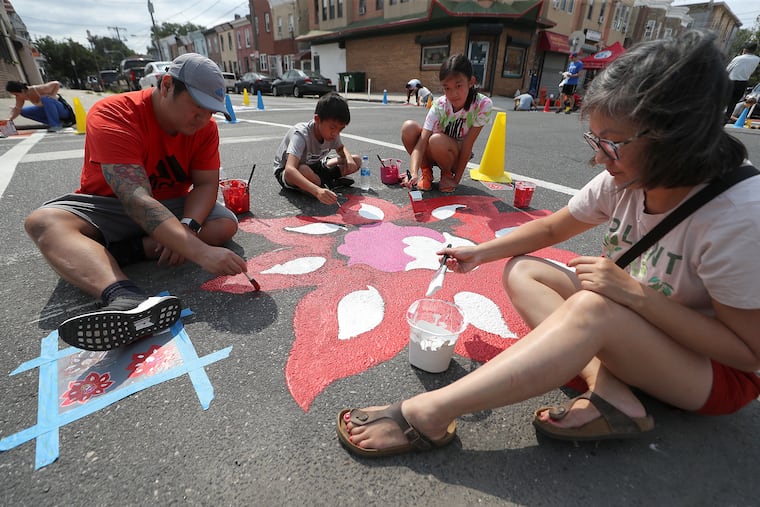 (Left to right) Dan, Jayden, Jasmine, and Kristina Chang work on a section of the mural at Seventh and Wolf Streets in Philadelphia on Sunday. The Lower Merion family joined other volunteers to paint a mural highlighting its Southeast Asian community and the area's immigrant-heavy population.