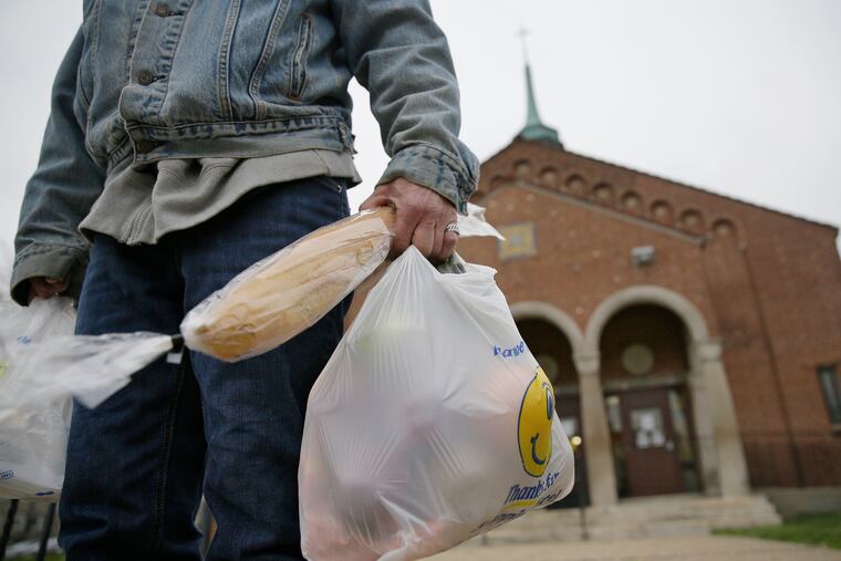 A man walks away with two bags of food and a fresh loaf of bread from the Feast of Justice food pantry at St. John’s Lutheran Church in the Mayfair section of Philadelphia. Such key parts of the social safety net are having a hard time meeting needs.