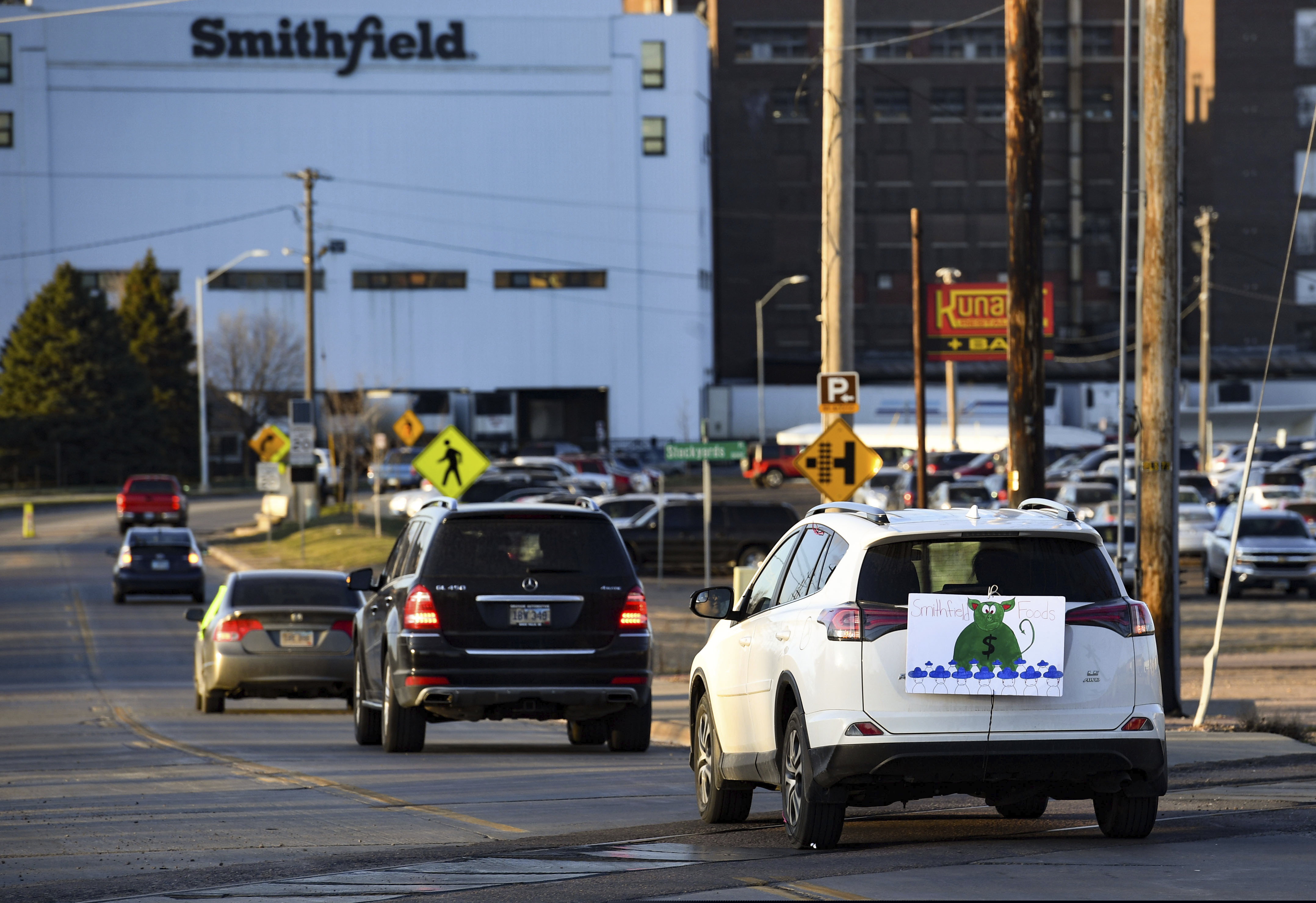 A sign depicting Smithfield Food, Inc. as a pig-shaped money bag is visible on the back of a car during a protest on behalf of employees calling for a safe and healthy workplace drives past Smithfield Foods, Inc. in Sioux Falls, S.D.
