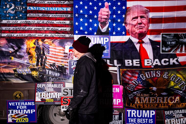 A rallygoer walks by a bus selling merchandise outside a Donald Trump event in Concord, N.H.