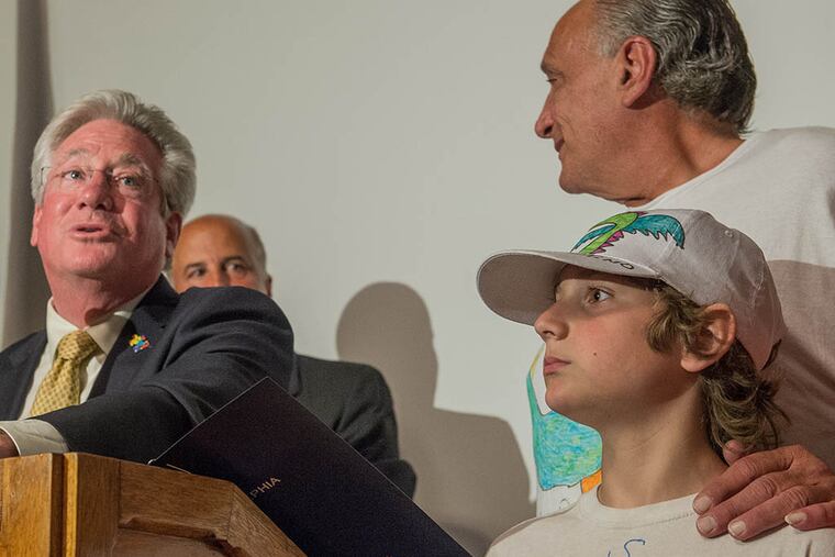Santino Sagliano (right) stands with his father, Mario, while Councilman Dennis O’Brien presents the boy with a certificate of recognition for his dragon T-shirt designs that raise awareness for autism. (Bryan Woolston/For The Inquirer)