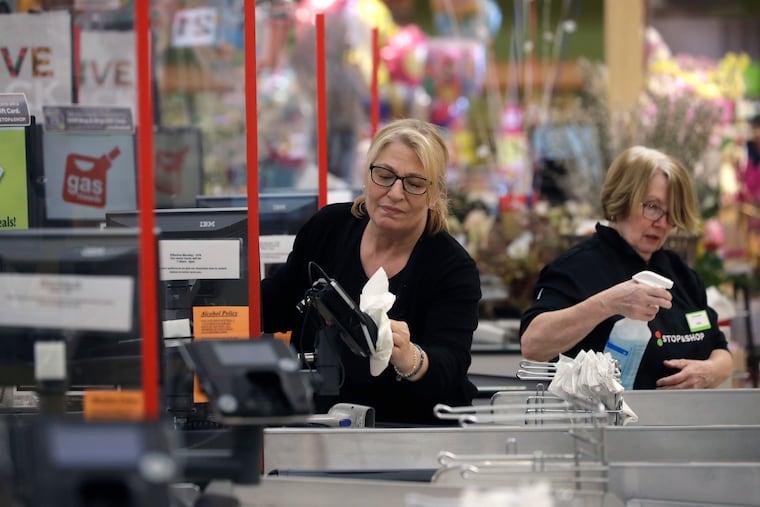 Cashiers at a grocery store sanitize a card reader and the checkout area, Thursday, March 26, 2020, in Quincy, Mass., as an extra precaution out of concern about the spread of the coronavirus. The new coronavirus causes mild or moderate symptoms for most people, but for some, especially older adults and people with existing health problems, it can cause more severe illness or death. (AP Photo/Steven Senne)