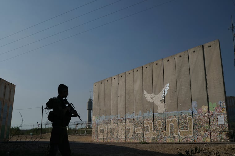 A member of the Israeli military stands next to a security wall with Hebrew writing reading "Path to Peace" at the Kibbutz Netiv Haasara near the border with the Gaza Strip, Israel, Friday. Members of the kibbutz were killed in the Hamas attacks on Oct. 7.