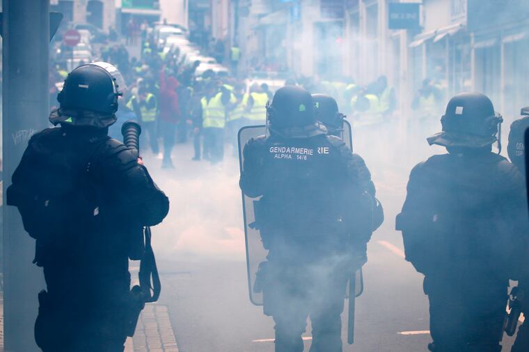 Demonstrators wearing yellow vests face riot police officers amid tear gas during a visit by French Foreign Minister Jean-Yves Le Drian in Biarritz, southwestern France, Tuesday, Dec. 18, 2018. Yellow vest protesters occupied dozens of traffic roundabouts across France even as their movement for economic justice appeared to be losing momentum on the fifth straight weekend of protests. (AP Photo/Bob Edme)