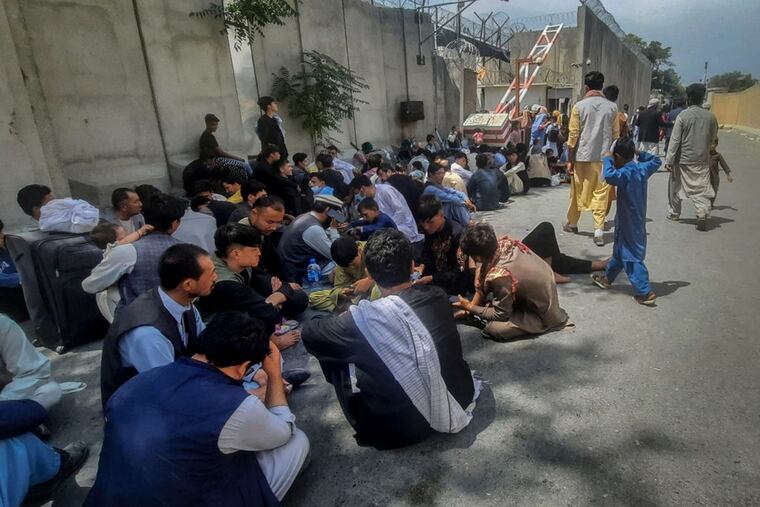 Afghan people sit outside the French embassy in Kabul on Tuesday waiting to leave Afghanistan.