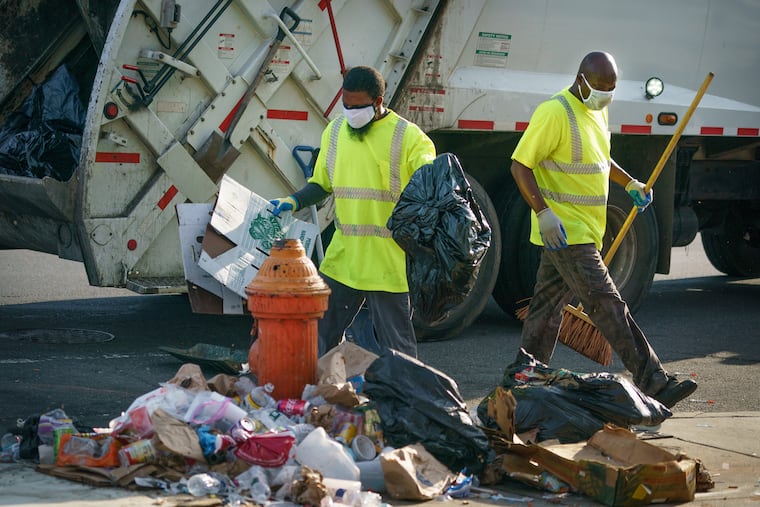 Philadelphia sanitation workers Rashan Purcell, left, and Lawrence Brown, right, collect trash on East Allegheny Avenue on July 27.