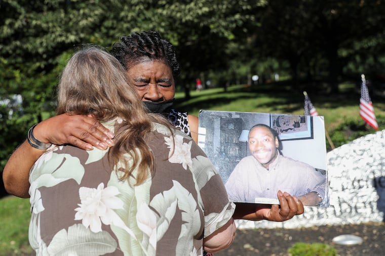 Elsie Goss Caldwell is hugged by a well-wisher as she holds a photo of her son, Kenneth Marcus Caldwell, who was 30 years old when he was killed in the 9/11 attack on the World Trade center, following a ceremony on the 20th anniversary of 9/11 at the Garden of Reflection in Lower Makefield, Pa.