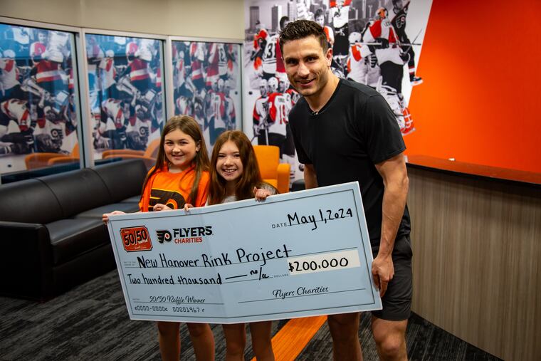 Flyers forward Garnet Hathaway presents Lilly Walter (left) and Natalie Van Druff (middle) with a donation to refurbish their local hockey rink.