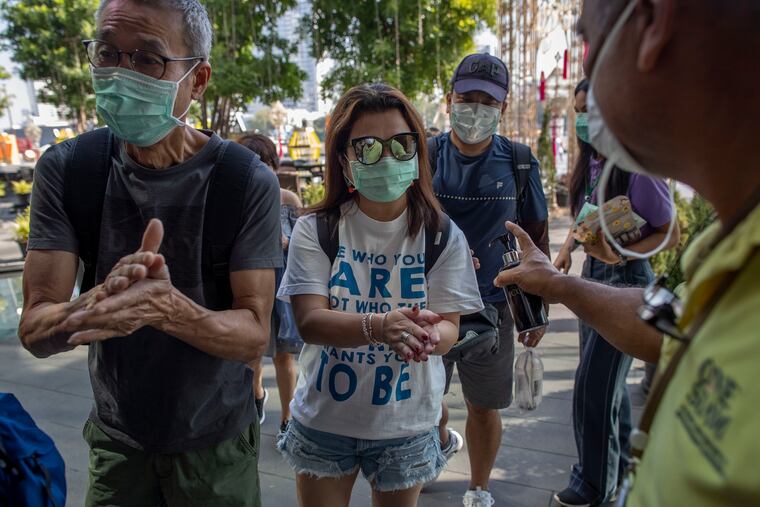 A doorman distributes hand sanitizing liquid for visitors at a luxury mall in Bangkok, Thailand.