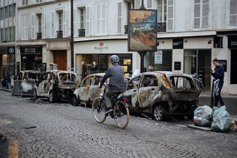 A man rides his bicycle past by charred cars, near the Arc de Triomphe, in Paris, Sunday, Dec. 2, 2018. A protest against rising taxes and the high cost of living turned into a riot in the French capital Saturday, as activists caused widespread damage and tagged the Arc de Triomphe with multi-colored graffiti during clashes with police. (AP Photo/Kamil Zihnioglu)
