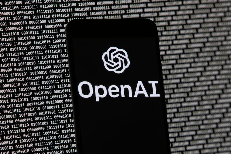 The OpenAI logo appears on a mobile phone in front of a computer screen with random binary data.