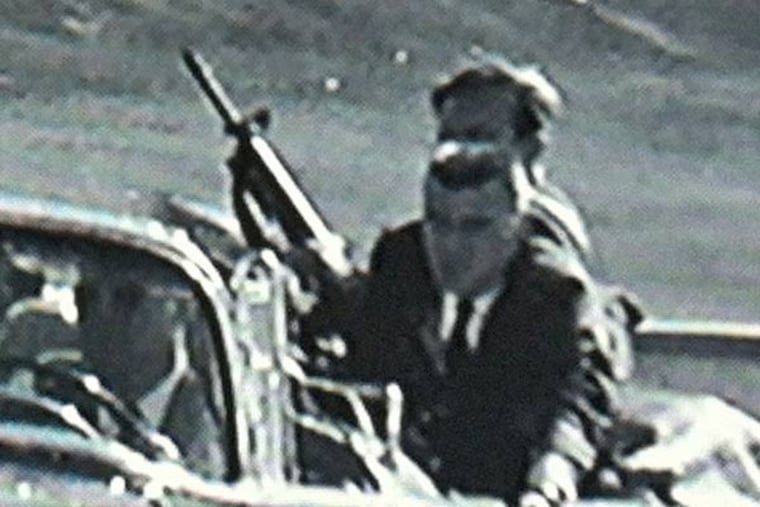 Secret Service agent George Hickey is seen brandishing a rifle as the limousine carrying a wounded President Kennedy, with agent Clint Hill on the back, speeds away from Dealey Plaza in Dallas on Nov. 22, 1963. One theory is that Hickey accidentally shot JFK.
