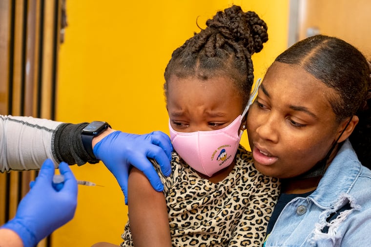 Jumayah Carter, 15, of West Philadelphia holds her sister, Mahilah Jones, 5, as she gets her shot from Children’s Hospital of Philadelphia primary care physician Katie McPeak during a COVID-19 vaccine event at the Philadelphia Zoo Dec. 14, 2021. It was her first shot. Carter had already been vaccinated.