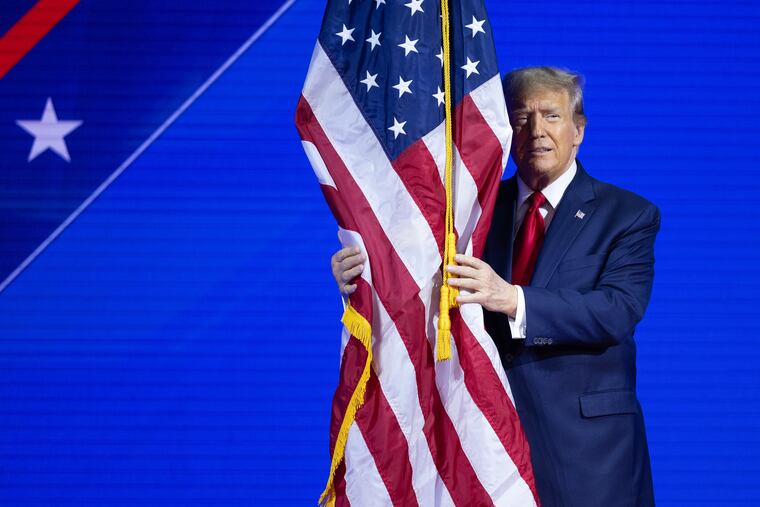 President Donald Trump hugs the American flag while walking onstage in 2024 in National Harbor, Maryland. (Tom Brenner/For the Washington Post )