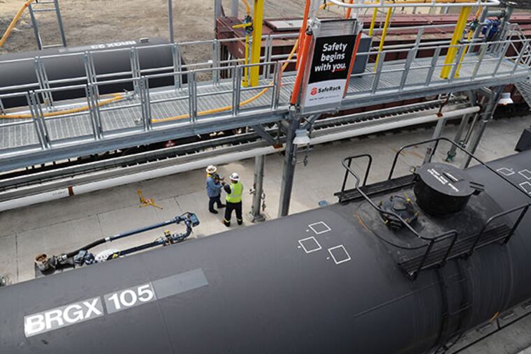 Workers wait for the train of empty oil tanker cars to be moved and full tankers brought into the depot at the Eddystone Railway Company complex in the old Exelon generating station in Eddystone, May 13, 2014. The company pumps oil from tank cars shipped from North Dakota into a holding tank and then transfers the oil to barges to be delivered to refineries along the East Coast. ( CLEM MURRAY / Staff Photographer )