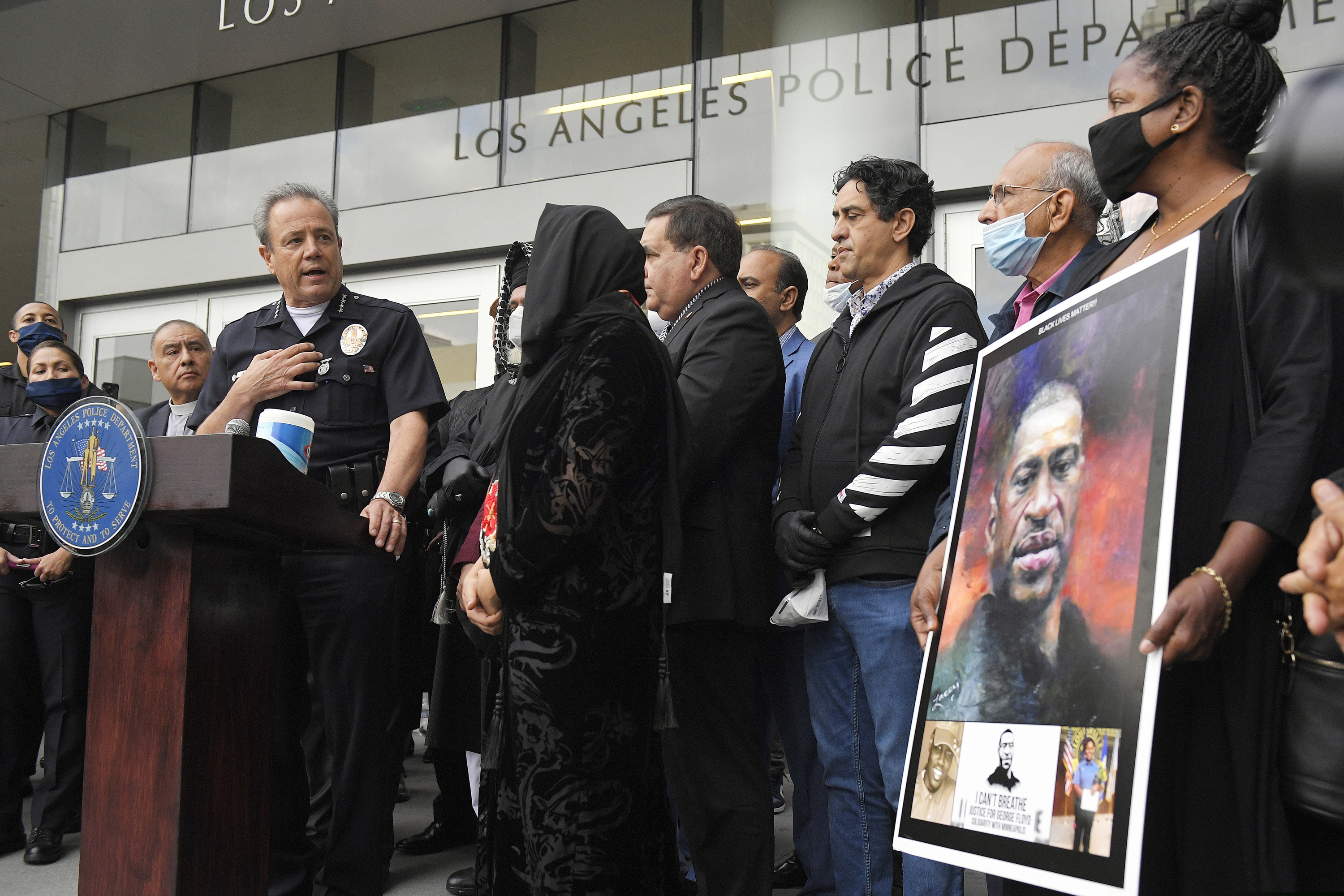 This June 5, 2020 photo shows Los Angeles police chief Michel Moore, left, speaking as someone holds up a portrait of George Floyd during a vigil at Los Angeles Police Department headquarters in Los Angeles.