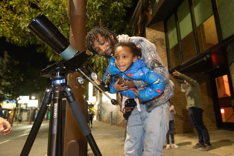 Isaac Cheeseboro lifts his daughter Isabella, 4, up to view Saturn in a telescope at 6th and South Streets in Philadelphia on Oct. 10, 2023.