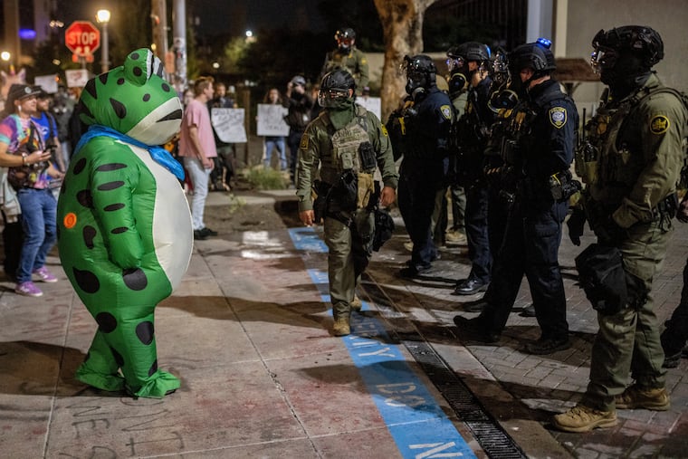 A protester in a frog costume stands in front of a line of federal law enforcement officers outside a United States Immigration and Customs Enforcement facility in Portland, Ore., Monday, Oct. 6, 2025.
