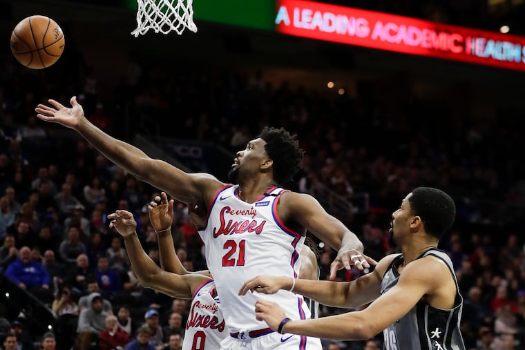 Sixers center Joel Embiid reaching for the basketball against Brooklyn Nets guard Spencer Dinwiddie on Feb. 20.