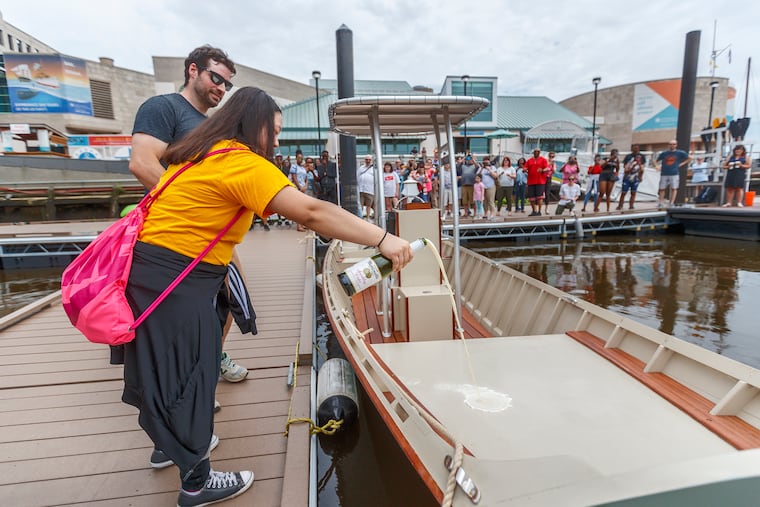 Vuochleng Kim, 15, from Bodine High School, pours sparkling apple cider to christen the JAWN, a boat that she and 70 other high school students built as part of a program at the Independence Seaport Museum that aims to expose underserved populations to science and technology.