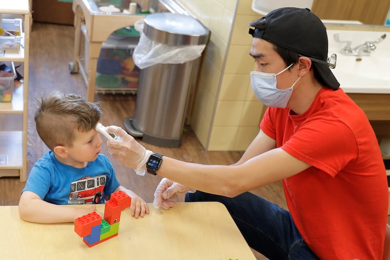 In this May 27, 2020, photo, Aaron Rainboth, a teacher at the Frederickson KinderCare day-care center in Tacoma, Wash., wears a mask as he takes the temperature of Benjamin Simpson, 4, after he complained of feeling hot following an outdoor play period but found it to be normal.