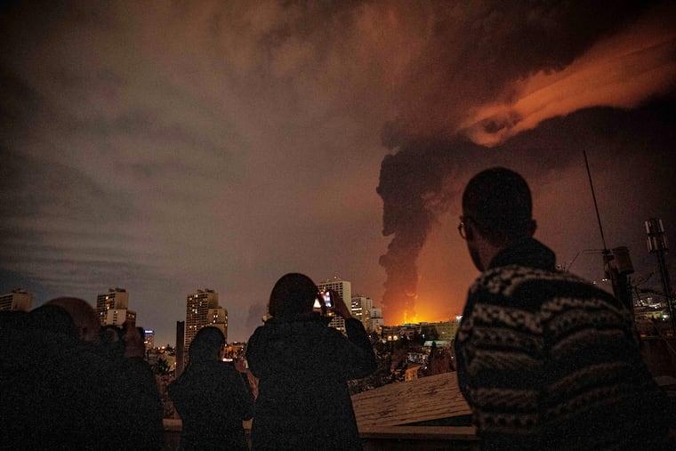 Residents look on and take pictures as flames and smoke rise from an oil storage facility struck as attacks hit the city during the U.S.–Israeli military campaign in Tehran, Iran, Saturday, March 7, 2026.