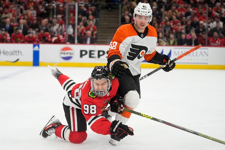 Blackhawks center Connor Bedard (left) trips over Flyers center Morgan Frost.