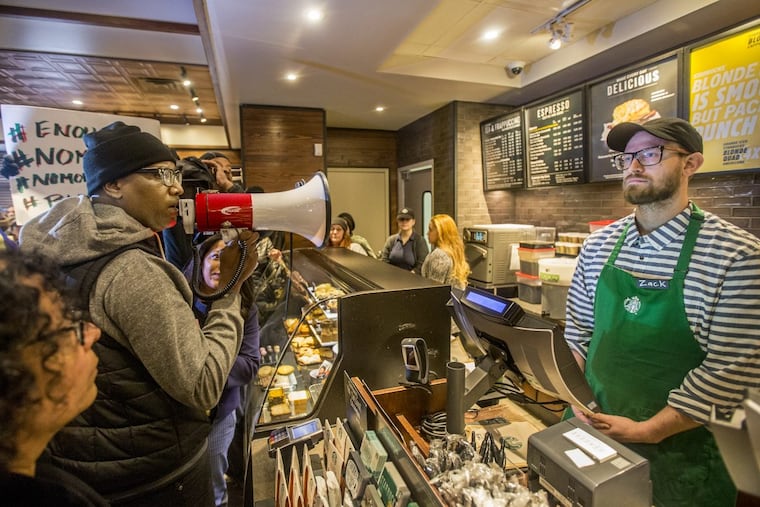 Black Lives Matter activist Asa Khalif, left, stands inside the Starbucks at 18th and Spruce, and over a bullhorn, demands the firing of the manager that called police, resulting in two black men being arrested.